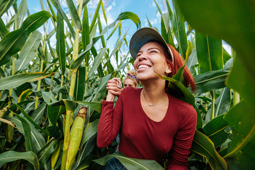 Two female farmers running through the corn field while holding hands and laughing with each other