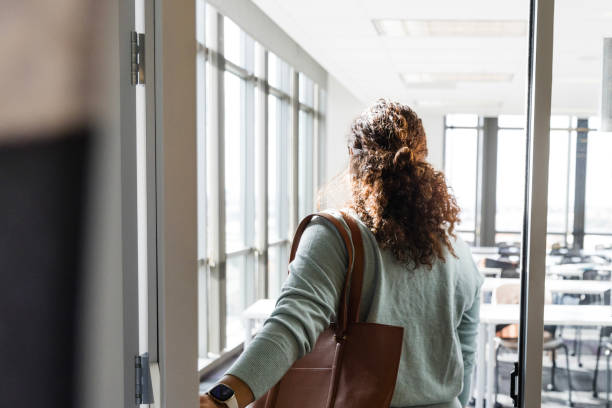 Rear view female teacher enter empty classroom