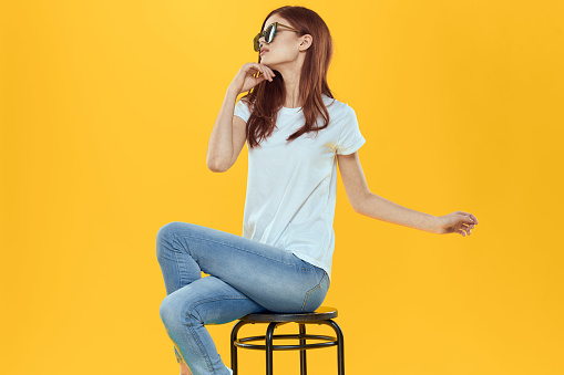 Pretty woman sits on a chair wearing sunglasses yellow background lifestyle. High quality photo