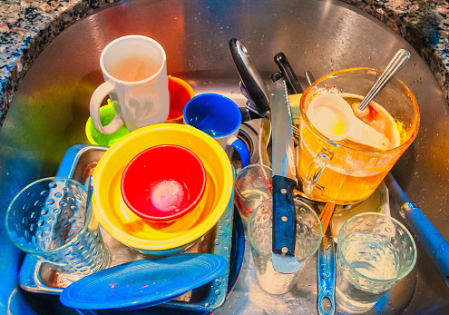 A pile of dirty dishes waiting to be washed in a kitchen sink.