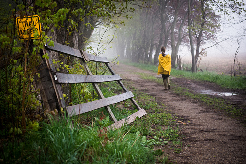 A female with a yellow raincoat takes a leisurely walk on a country road on a foggy day.
