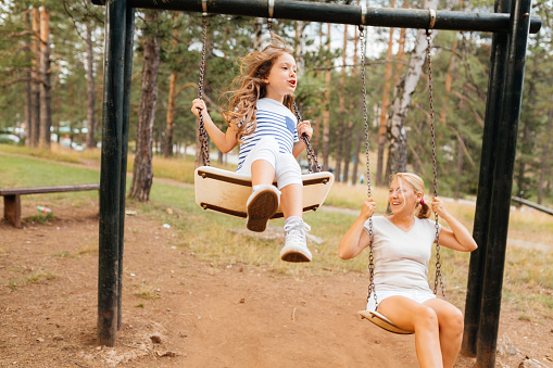 Mother and daughter having a great time together ,swinging on a swing in the park