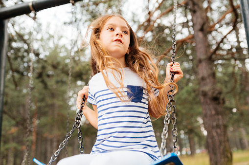 Cheerful girl having fun swinging in the park