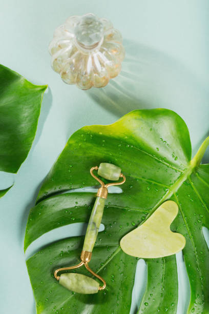 istock Green jade face roller and gua sha scraper with leaves on light blue background 2131101545