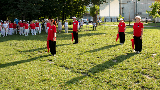 Dnepr, Ukraine - 06.21.2021: Group of elderly people doing health and fitness gymnastics with umbrellas in the park.