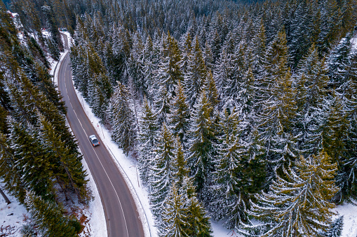 Aerial view of a car driving on a highway in a snow capped mountain.