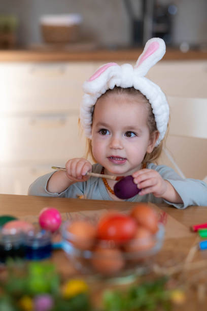 little girl sits at the table and paints Easter eggs with Easter paint, smile, grass, colorful colors