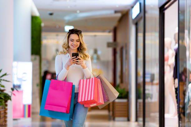 istock Effortless Shopping: Woman Smiles, Typing on Phone While Carrying Bags 2131216769
