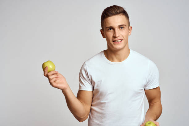 istock a guy with apples in his hands on a light background in a white t-shirt gesticulate with his hands smile 2131222495