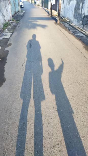 Human and dog shadows stretch across sunlit tiled sidewalk, capturing urban companionship, leisurely walk, warm summer day and the quiet bond between owner and pet