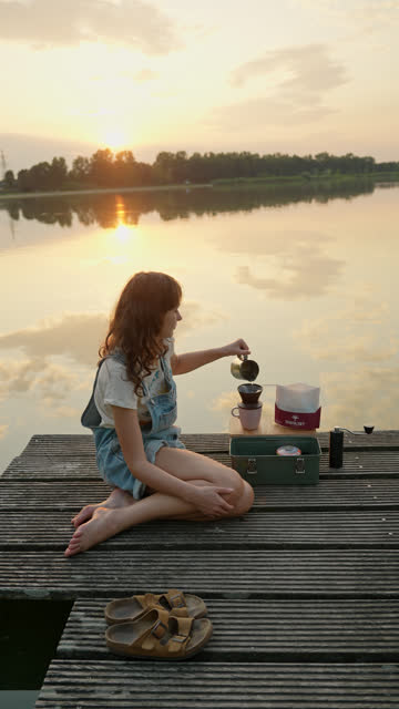 Woman sitting near the lake  and brewing coffee at sunset