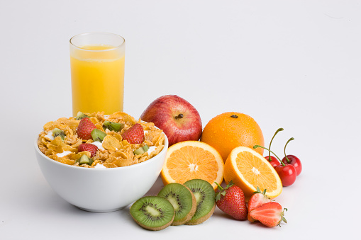 Breakfast cereal: Corn flakes with milk and fruits, orange juice, apple, orange, cherries, strawberries and kiwis.