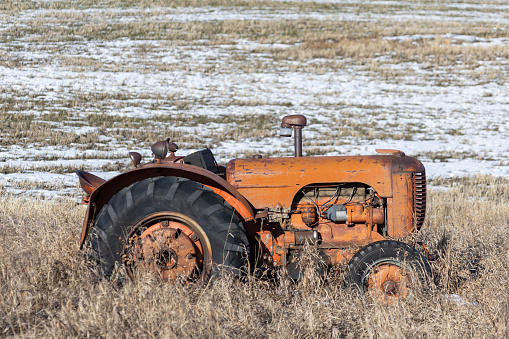 Outdoor rural scene of an antique tractor at the edge of an agricultural field with a light dusting of snow and dry brown grass.