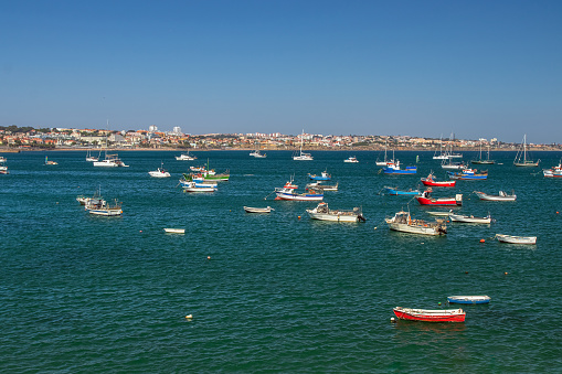 View over the bay of Cascais, Portugal, in front of the Ribeira beach jetty where several fishing and leisure boats are anchored.