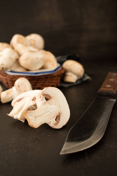 Cut champignon and some mushrooms in a basket with a knife on a black wooden table