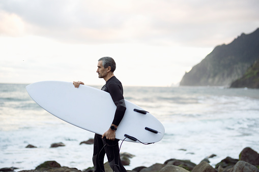 Mature man goes surfing at sunrise. Getting away from it all.