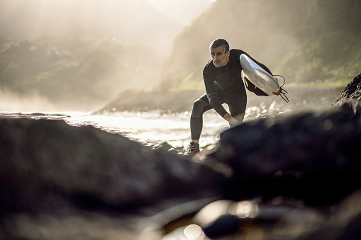 Mature man goes surfing at sunset. Getting away from it all.