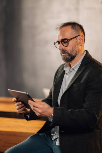 istock Serious mature executive with tablet sitting on desk at modern office. 2131378987
