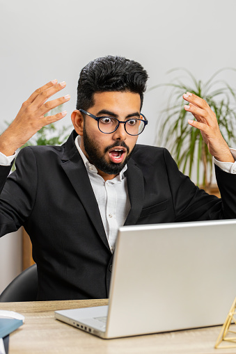 Displeased Indian businessman programmer software developer working on laptop loses becoming surprised by bad news results, fortune loss fail at home office. Deadline, bankruptcy. Freelancer man