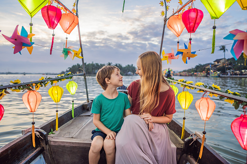 Happy family Mother and son of travelers ride a national boat on background of Hoi An ancient town, Vietnam. Vietnam opens to tourists again after quarantine Coronovirus COVID 19.