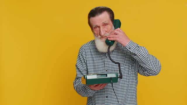 Senior man talking on wired landline vintage telephone, advertising proposition of conversation