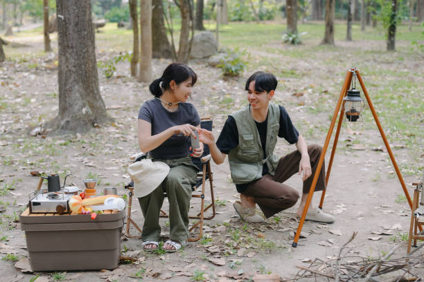 istock Asian couple clinking coffee mug together at camp side, They feeling relaxed and refreshing while camping in the nature. Recreation 2131489652