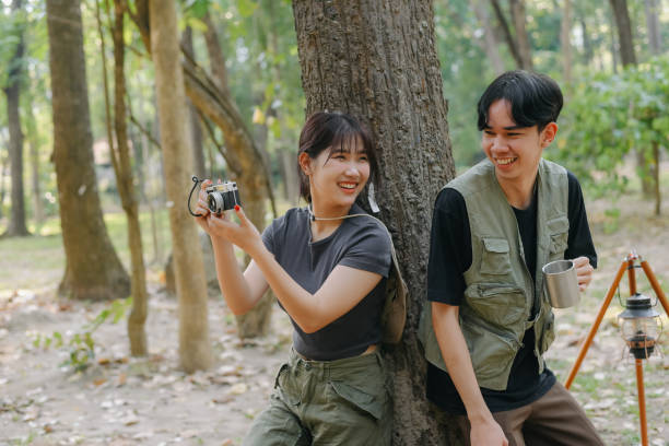 istock Asian couple clinking coffee mug together at camp side, They feeling relaxed and refreshing while camping in the nature. Recreation 2131490174