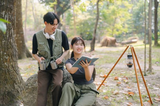 istock Asian couple clinking coffee mug together at camp side, They feeling relaxed and refreshing while camping in the nature. Recreation 2131490192