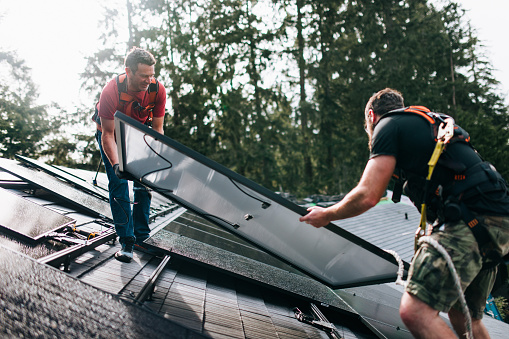 A professional solar panel crew installs panels on the roof of a house in Washington state, USA.  Green environmentally friendly energy.