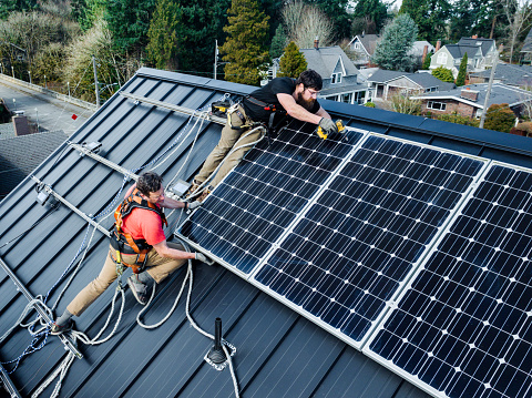 A professional solar panel crew installs panels on the roof of a house in Washington state, USA.  Green environmentally friendly energy.  Drone point of view.