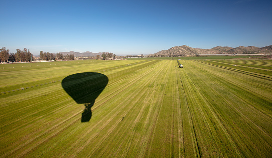 Shadow of hot air balloon over freshly cut alfalfa field seen from aerial viewpoint in Menifee southern California United States
