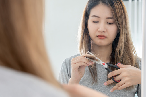 Asian woman very sad and upset looking at damaged hair, hair loss, hair thinning problem, vitamin deficiency, baldness, postpartum, biotin, zinc, menstrual or endocrine disorders, hormonal imbalance