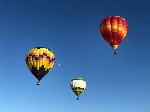 Hot air balloon trio with the moon over blue sky