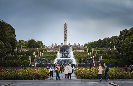 View of Vigeland Sculpture Park on rainy summer day with visitors looking at sculptures, fountain and column