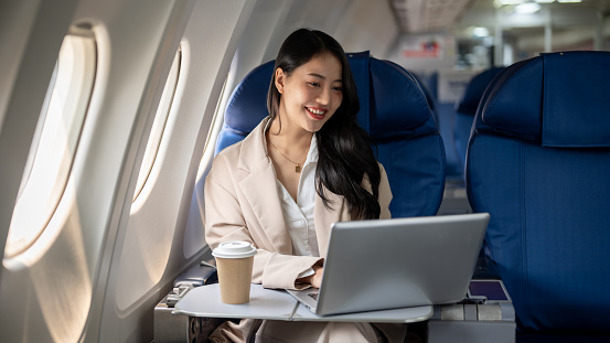 An attractive, successful Asian businesswoman or female CEO in a business suit is working on her laptop computer during the flight for her business trip to another city. airplane, transportation
