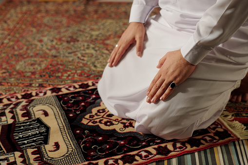 High angle view of unrecognizable young Muslim man wearing white thobe doing namaz on prayer rug, copy space