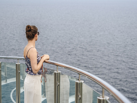 Cute woman standing on the empty deck of a cruise liner against the backdrop of sea waves. Sunny, clear day. Closeup, outdoor. Vacation and travel concept