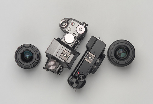 Two modern digital mirrorless cameras with lenses on a gray background. Top view