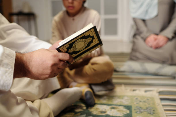 Selective focus closeup of unrecognizable Muslim man reading Quran surah at family gathering at home, copy space