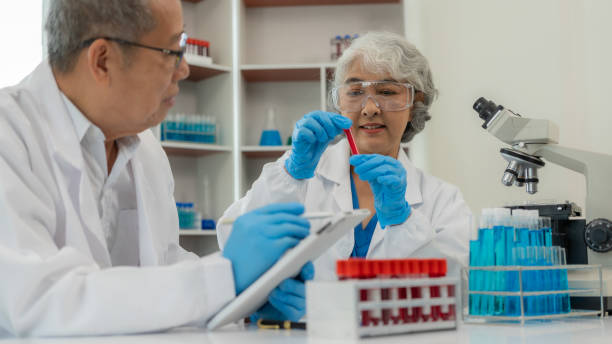 dwoje starszych azjatów i azjatek jest naukowcami prowadzącymi badania w dziedzinie biologii i chemii. para w okularach i patrząca pod mikroskop w laboratorium ze szklanymi rurkami na stole - test cricket zdjęcia i obrazy z banku zdjęć