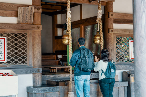 Two tourists visiting and praying at a Japanese shrine in Okayama Prefecture while on vacation