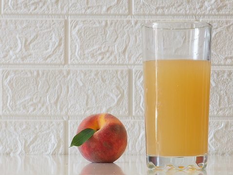 Glass of peach juice and peach fruits on white wooden table