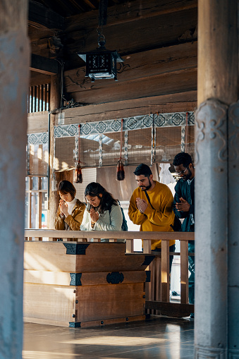 Four diverse mid adult tourists praying at a shrine while vacationing in Japan
