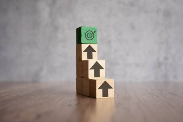 A stack of wooden blocks with arrows pointing upwards and target board. A stack of wooden blocks with arrows pointing upwards and target board. Mission, focus, ladder of success concept. pursuit concept stock pictures, royalty-free photos & images
