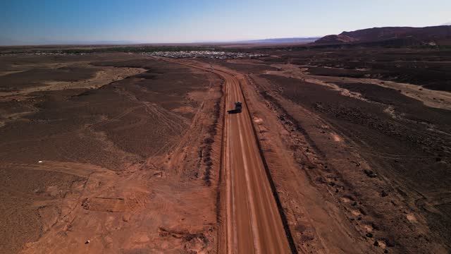 Truck driving on dusty road through Chilean desert landscape, aerial shot in bright daylight