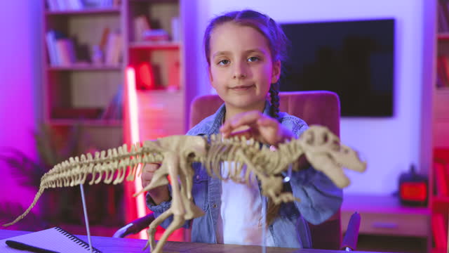 Happy preschool child gluing bones making model of tyrannosaurus at evening home