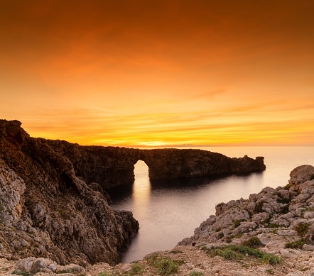 A view of the landmark stone arch of Pont d'en Gil on Menorca Island just after sunset