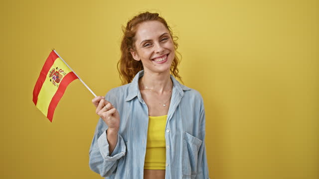 Cheerful woman holding spanish flag against yellow background expresses patriotism and positivity.