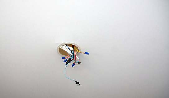 Exposed electrical wires protrude from a junction box in a ceiling, waiting to be connected to a fixture. The wires, secured with blue connectors, hint at ongoing electrical work