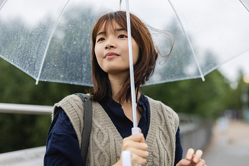 portrait of asian woman under her transparent umbrella while the wind moves her hair
